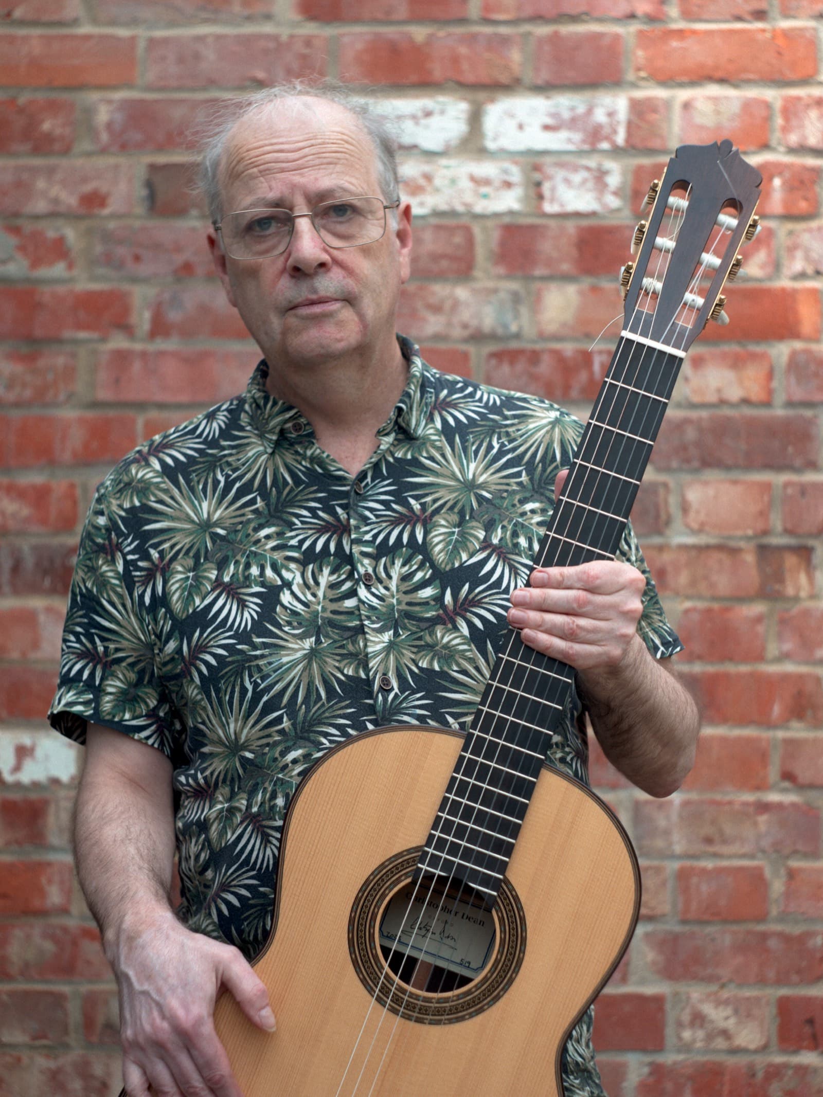 Julian Masters holding a Christopher Dean classical guitar in front of a red-brick wall